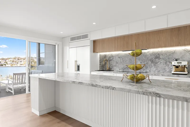 Transform your home with Dura Group's luxury kitchen upgrades. This beautifully designed kitchen features a spacious marble island, sleek cabinetry, and modern fixtures, all bathed in natural light from wide glass doors that lead to a scenic outdoor view. Dura Group, a Sydney-based family-owned construction company, specializes in home renovations across the Sutherland Shire, Bayside, Inner West, Georges River, and Randwick regions. With over 27 years of experience, Managing Director Mark ensures each project prioritizes time efficiency, budget-conscious planning, and consistently high-quality builds. Our homeowner-first approach focuses on trust, transparency, and customized building solutions, enhancing both functionality and aesthetics without sacrificing quality. Whether it's kitchen upgrades, bathroom remodels, or upper-storey additions, our expert team communicates clearly, ensuring your vision is realized while staying on schedule and budget. Experience the ultimate kitchen transformation and bring elegance and practicality to your home. Contact Dura Group today for a free consultation and make your dream home a reality. Act now to create a space that's both beautiful and functional.
