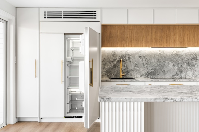 Explore the elegance of this luxury kitchen renovation featuring stunning marble accents and modern, minimalist design by Dura Group. Located in Sydney, our family-owned building company excels in creating upscale living spaces tailored to your unique style. The open refrigerator seamlessly integrates into custom cabinetry, offering both functionality and contemporary aesthetics. With over 27 years of construction experience, our Managing Director, Mark, leads a skilled team dedicated to delivering premium kitchen upgrades across the Sutherland Shire, Bayside, Inner West, Georges River, and Randwick regions. This striking kitchen combines sleek white cabinetry, textured marble countertops, and a sophisticated backsplash, enhancing aesthetics while maintaining practical use. The gold fixtures add a touch of opulence, perfectly complementing the design's modern elegance. Dura Group's commitment to time efficiency, budget-conscious planning, and transparent communication ensures each project meets client expectations without compromising on quality. Elevate your living space with a trusted Sydney renovation expert who prioritizes homeowner satisfaction. Discover the Dura Group difference today and transform your kitchen into a stunning masterpiece. Contact us now to start your renovation journey!