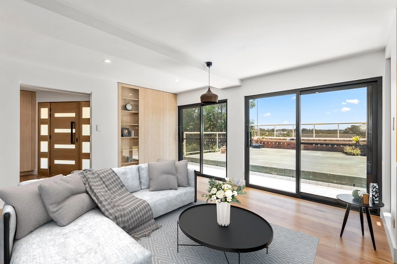 Discover the elegance and functionality of a beautifully renovated living room by Dura Group, a leading family-owned building company in Sydney. With over 27 years of experience, Managing Director Mark ensures excellence in home renovations throughout the Sutherland Shire, Bayside, Inner West, Georges River, and Randwick regions. This stunning living space features modern sliding glass doors that fill the room with natural light, seamlessly blending indoor and outdoor areas. A cozy, stylish sofa with soft grey cushions and a chic plaid throw enhances comfort. The room's modern aesthetic is complemented by a sleek black coffee table with a decorative floral arrangement. A contemporary light fixture adds a touch of sophistication while built-in shelving offers practical storage solutions. Prioritising time efficiency and budget-conscious planning, Dura Group delivers high-quality projects tailored to homeowner needs. Trust and transparency are at the heart of our process, ensuring a seamless renovation experience. Transform your home with our expert team. Contact Dura Group today to start your next home renovation project and experience the difference we bring!