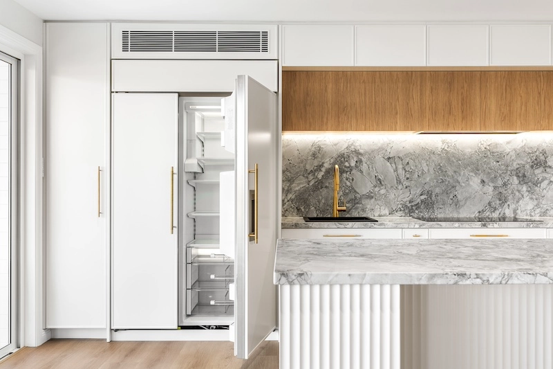 Explore the elegance of this luxury kitchen renovation featuring stunning marble accents and modern, minimalist design by Dura Group. Located in Sydney, our family-owned building company excels in creating upscale living spaces tailored to your unique style. The open refrigerator seamlessly integrates into custom cabinetry, offering both functionality and contemporary aesthetics. With over 27 years of construction experience, our Managing Director, Mark, leads a skilled team dedicated to delivering premium kitchen upgrades across the Sutherland Shire, Bayside, Inner West, Georges River, and Randwick regions. This striking kitchen combines sleek white cabinetry, textured marble countertops, and a sophisticated backsplash, enhancing aesthetics while maintaining practical use. The gold fixtures add a touch of opulence, perfectly complementing the design's modern elegance. Dura Group's commitment to time efficiency, budget-conscious planning, and transparent communication ensures each project meets client expectations without compromising on quality. Elevate your living space with a trusted Sydney renovation expert who prioritizes homeowner satisfaction. Discover the Dura Group difference today and transform your kitchen into a stunning masterpiece. Contact us now to start your renovation journey!